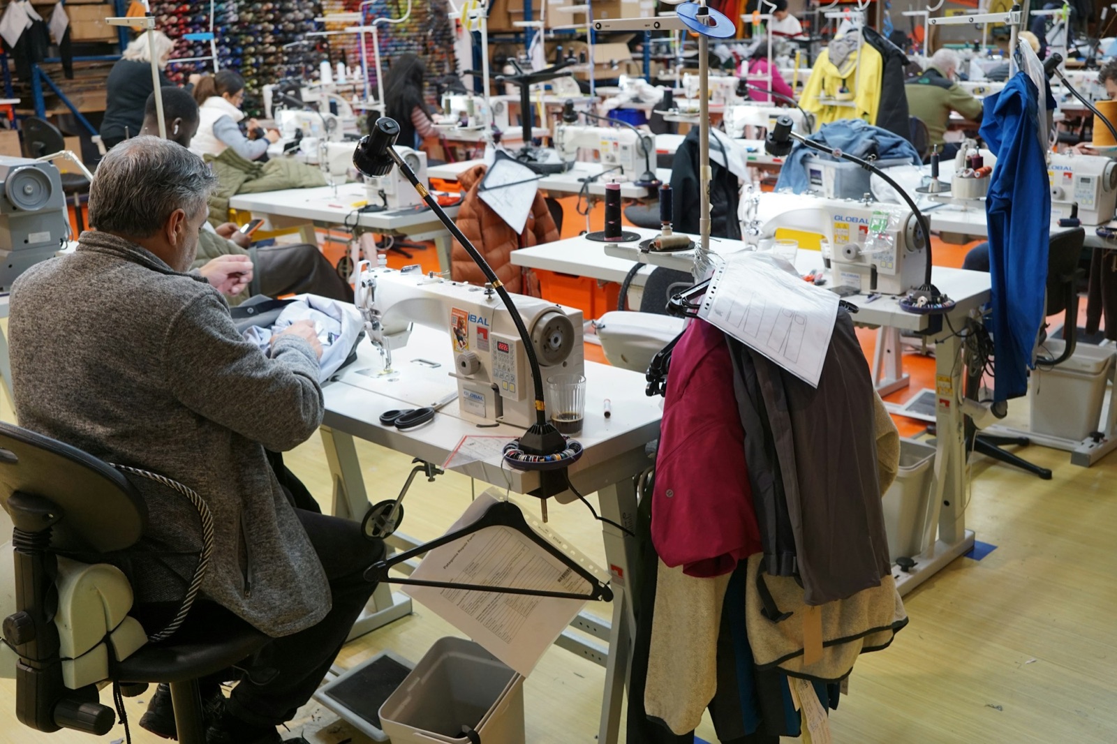 Rows of industrial sewing machines with workers stitching garments in a cut-and-sew workshop
