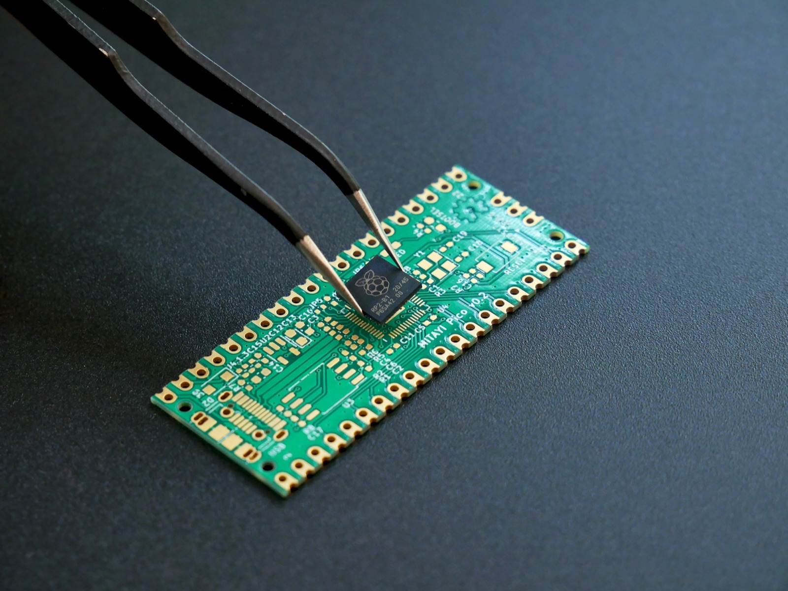 Tweezers placing a microchip onto a green printed circuit board