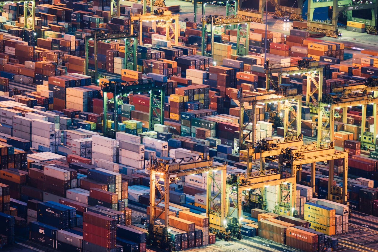 Aerial view of stacked shipping containers and gantry cranes in a container yard at night