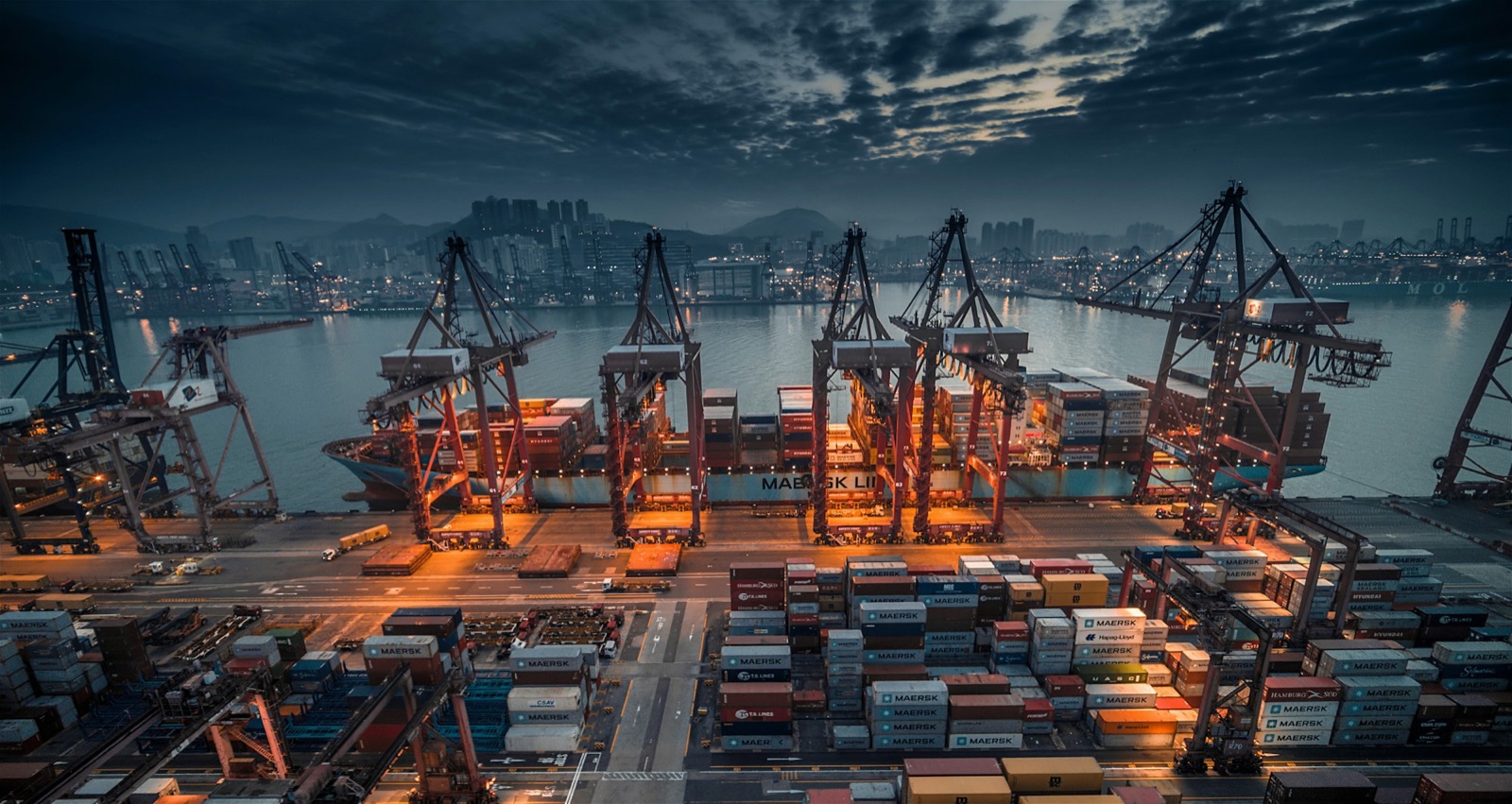 Container ship being loaded by gantry cranes at a Hong Kong container terminal at dusk
